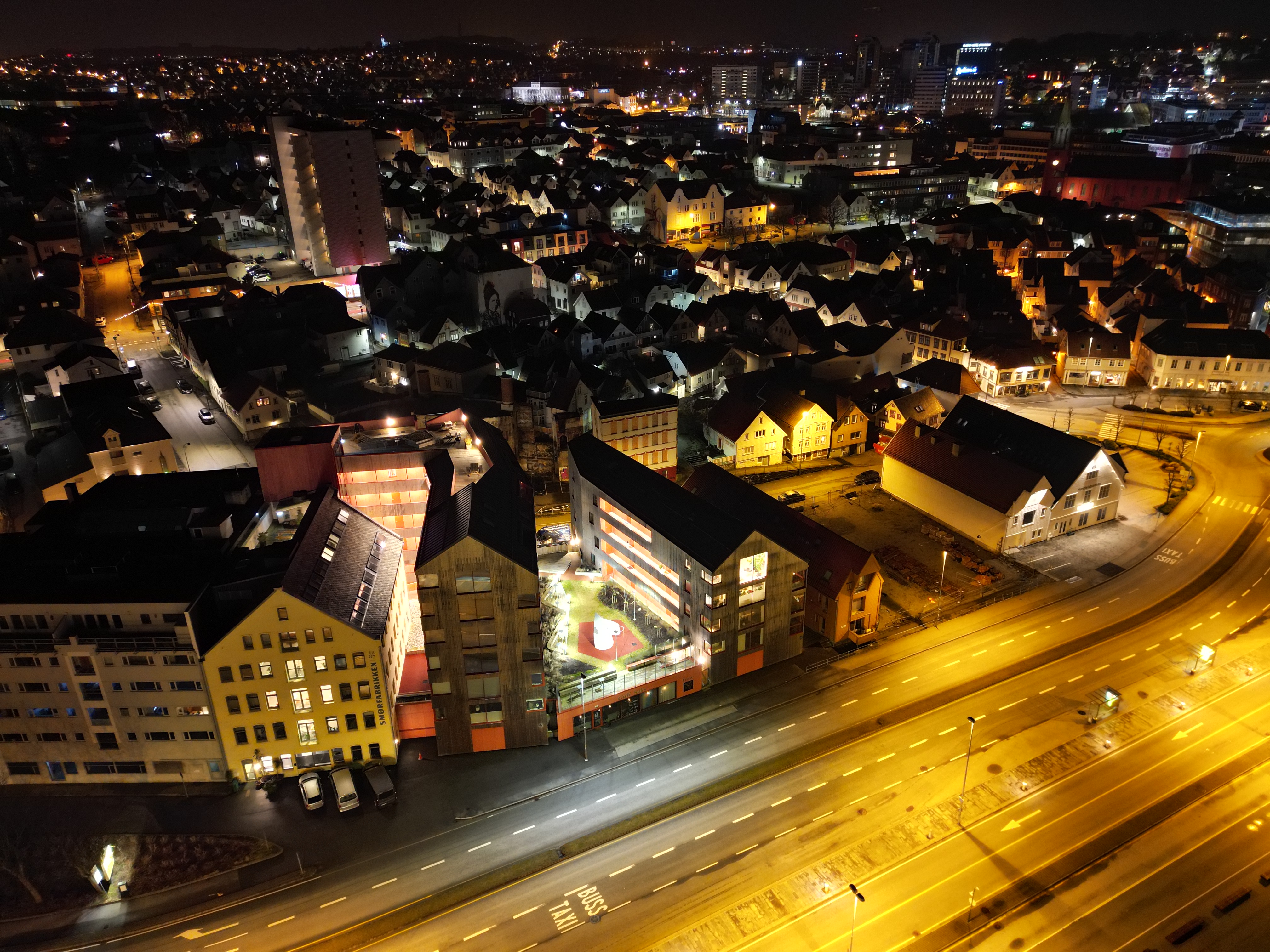 Skutene fotografert fra luften om natten — leilighetsbyggene med opplyst gårdsrom og Smørfabrikken til venstre, med Stavanger sentrum og Vågen-området i bakgrunnen